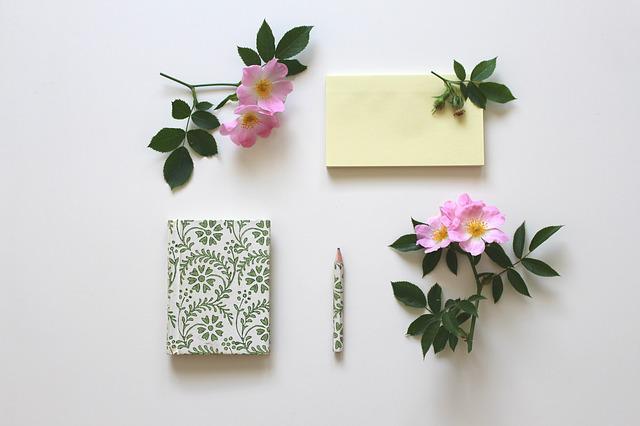 bílý zápisník se zeleným květinovým vzorem a stejně vzorovanou tužkou, položené na stole spolu s květy divoké růže